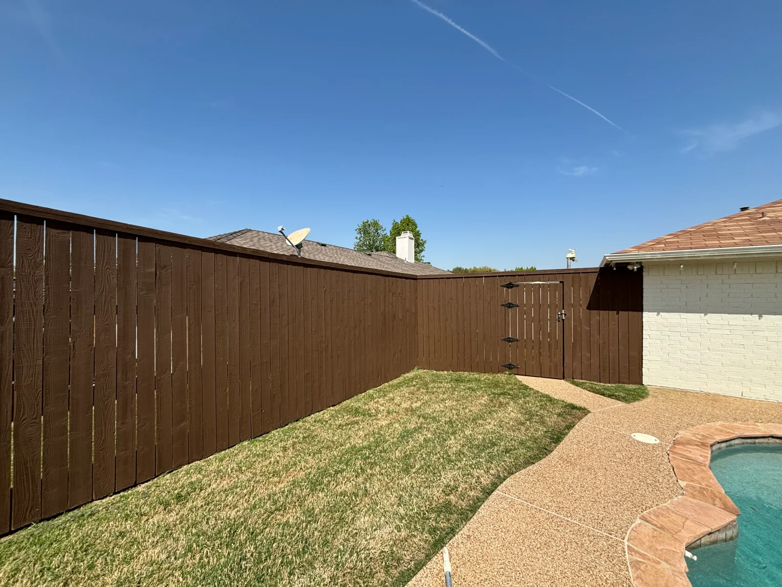 Dark brown stained vertical board fence with pool deck and landscaping