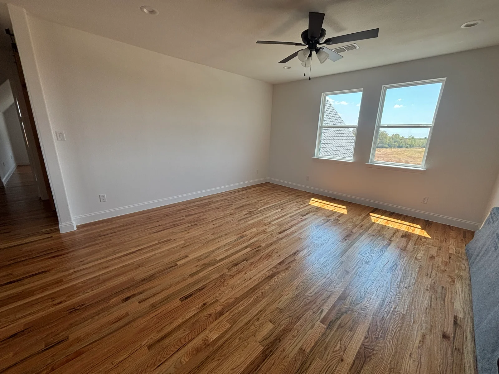 Freshly painted white bedroom walls and ceiling with hardwood floors and dual windows