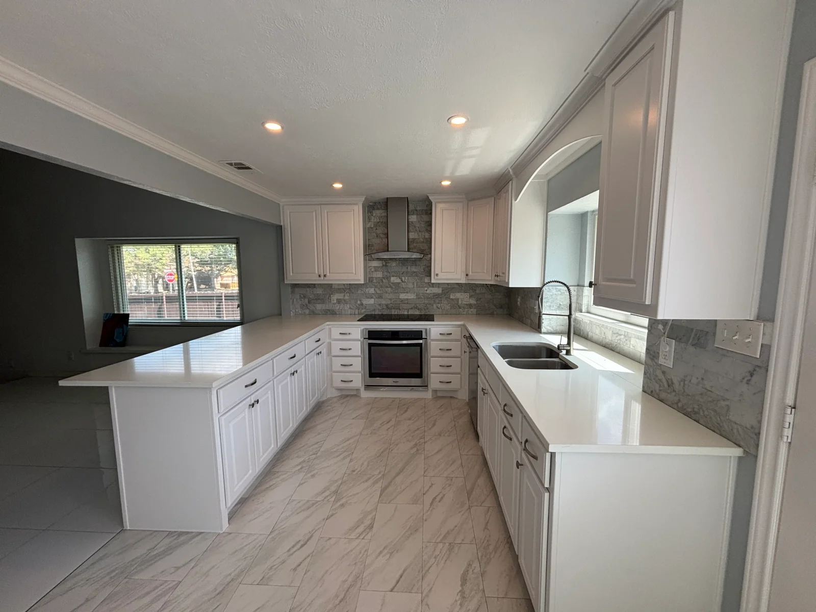 White painted kitchen cabinets with gray accent wall, stone backsplash, and recessed lighting