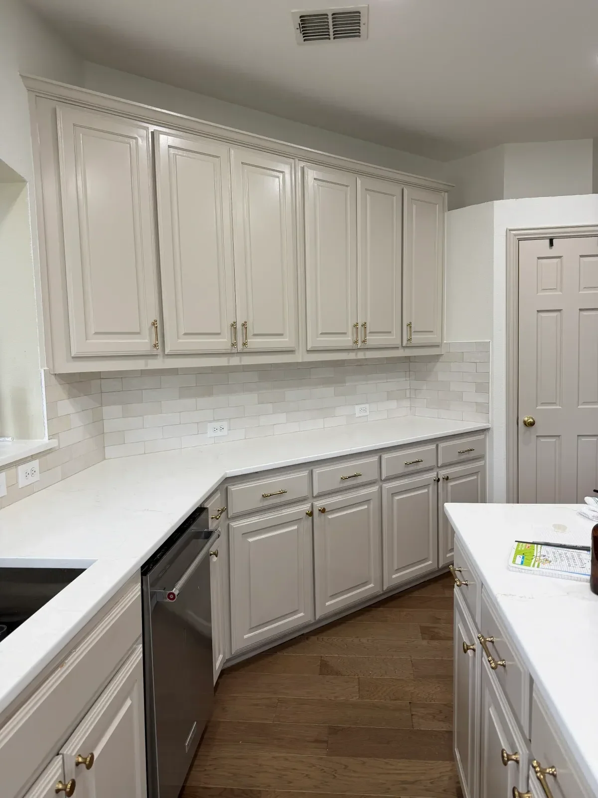White painted kitchen cabinets with raised panels, brass hardware, black countertops, and subway tile backsplash