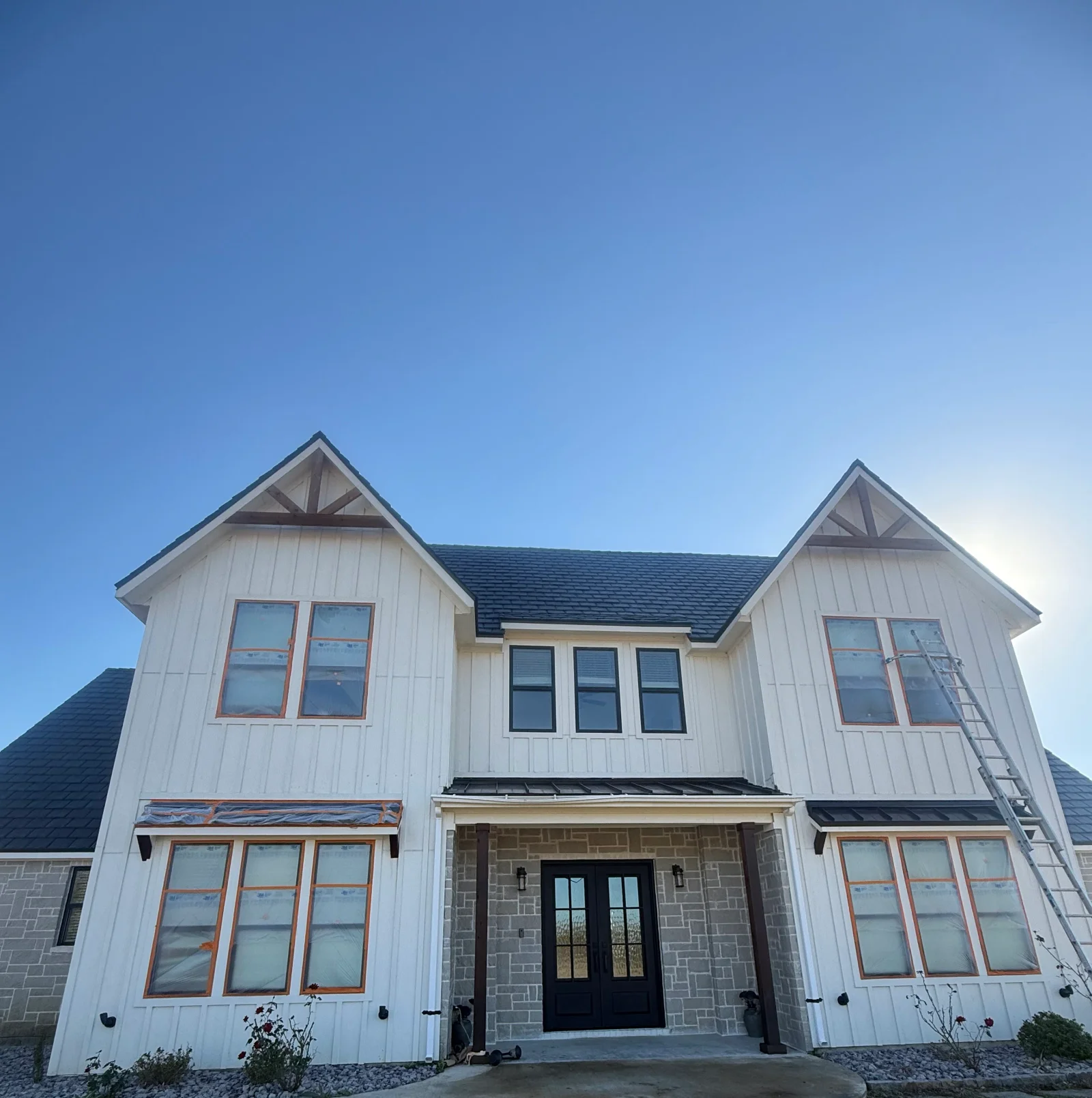 White vertical siding farmhouse with dark roof, copper-trimmed windows, and stone entry facade